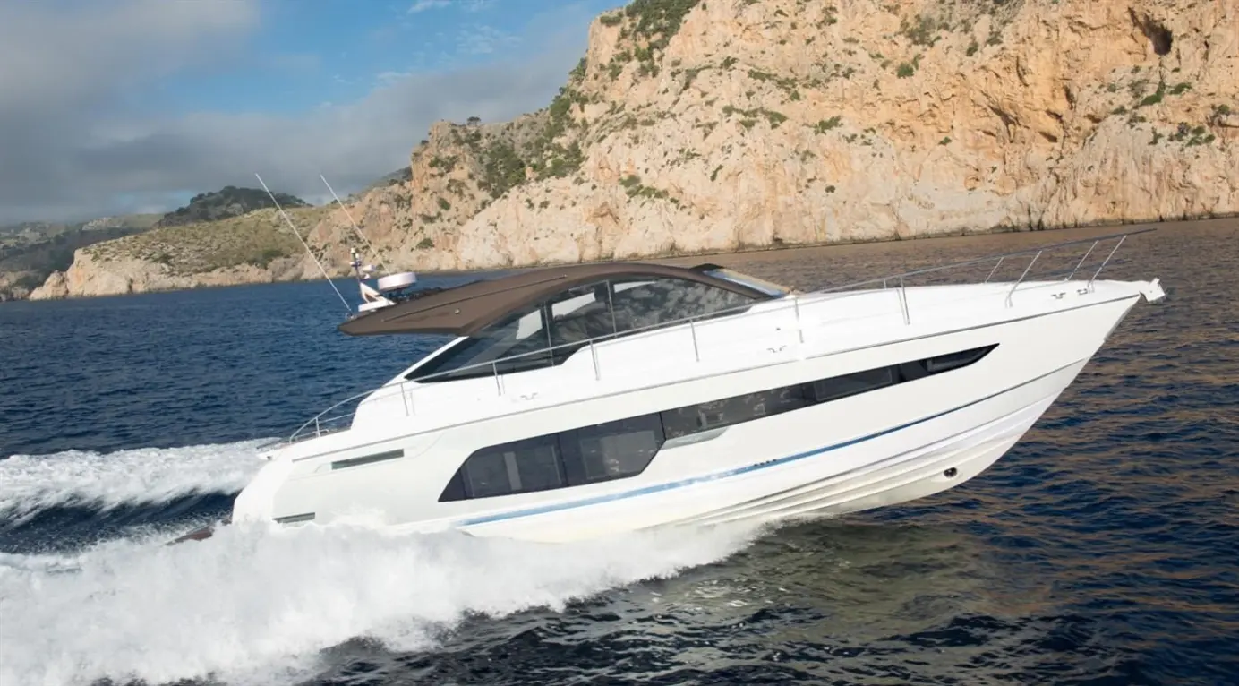 A sleek white motorboat cruising across calm waters, with rocky cliffs and greenery in the background.